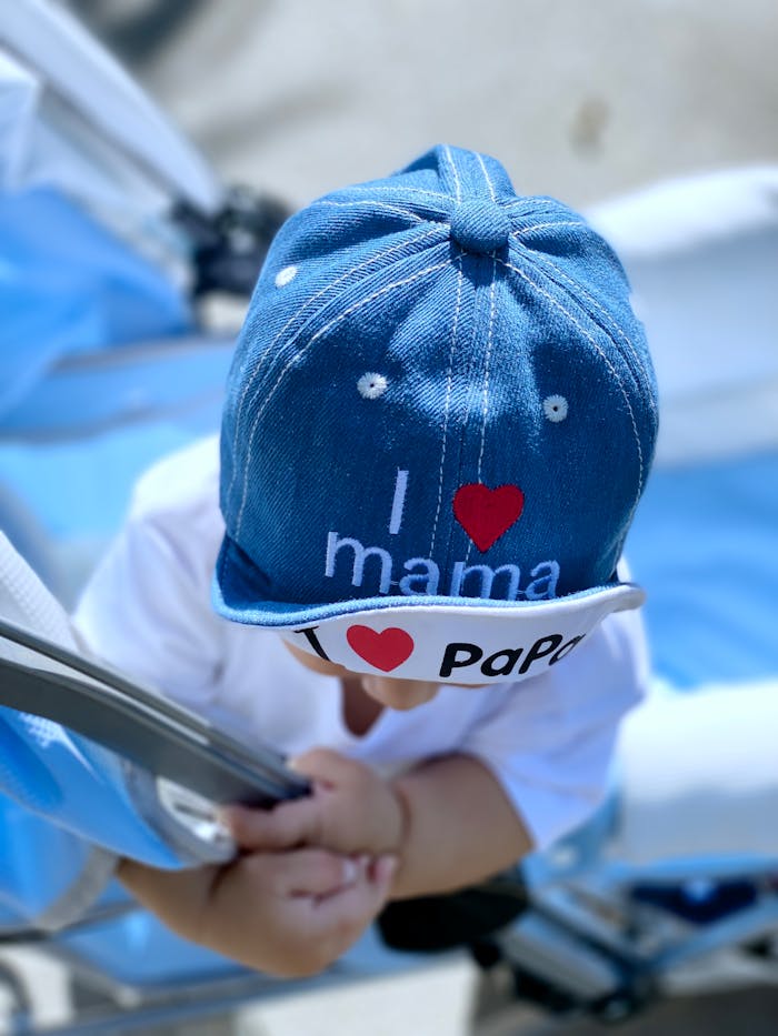 Cute baby wearing a blue hat with 'I love mama' and 'I love papa' printed, sitting in a pram.