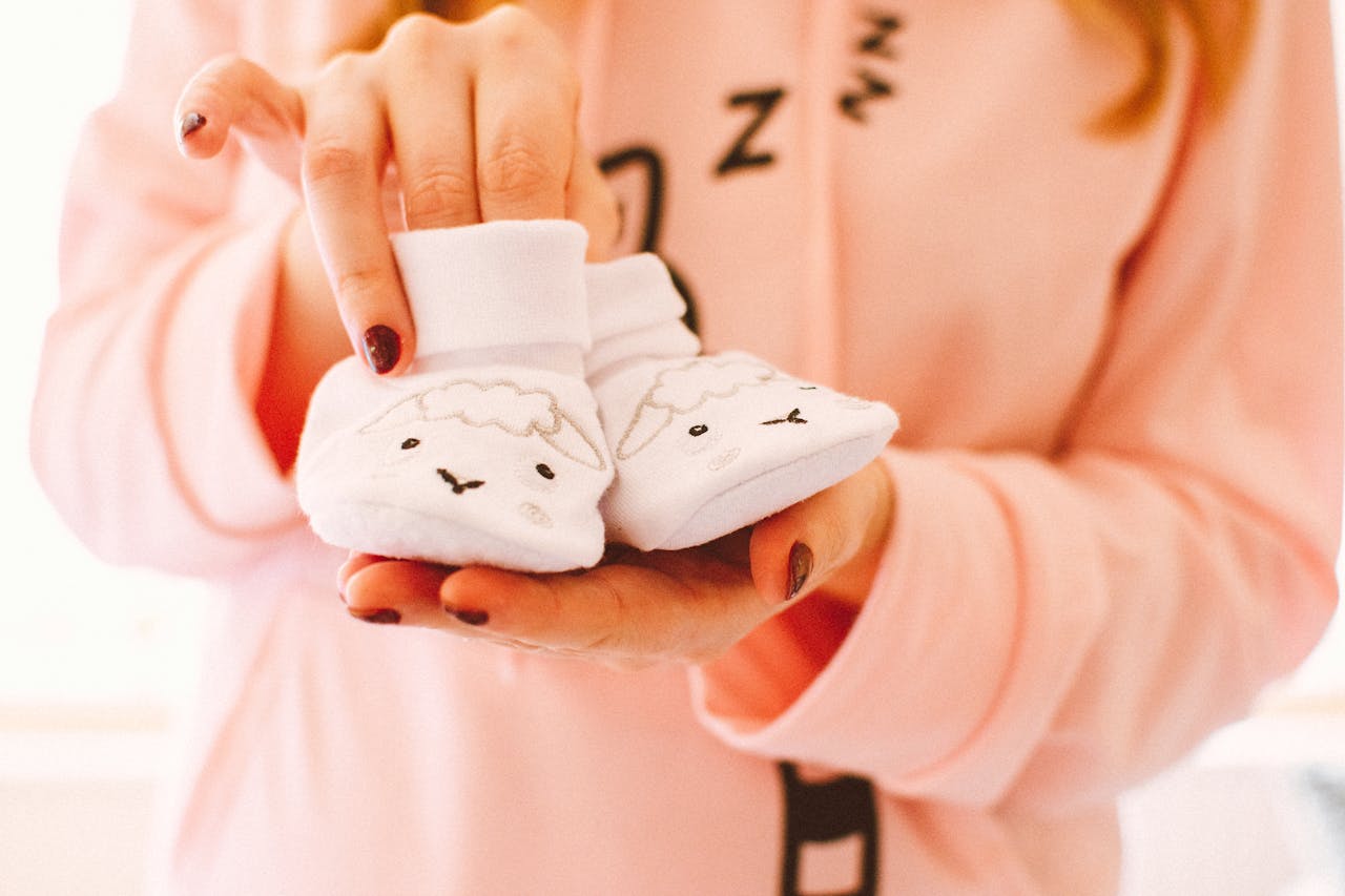 A woman in pink holds cute baby shoes with sheep designs, symbolizing warmth and love.