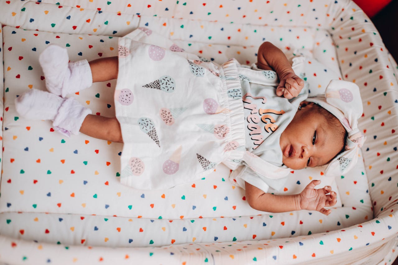 Cute baby lying on a colorful heart-patterned blanket, wearing pastel clothes and a headband.