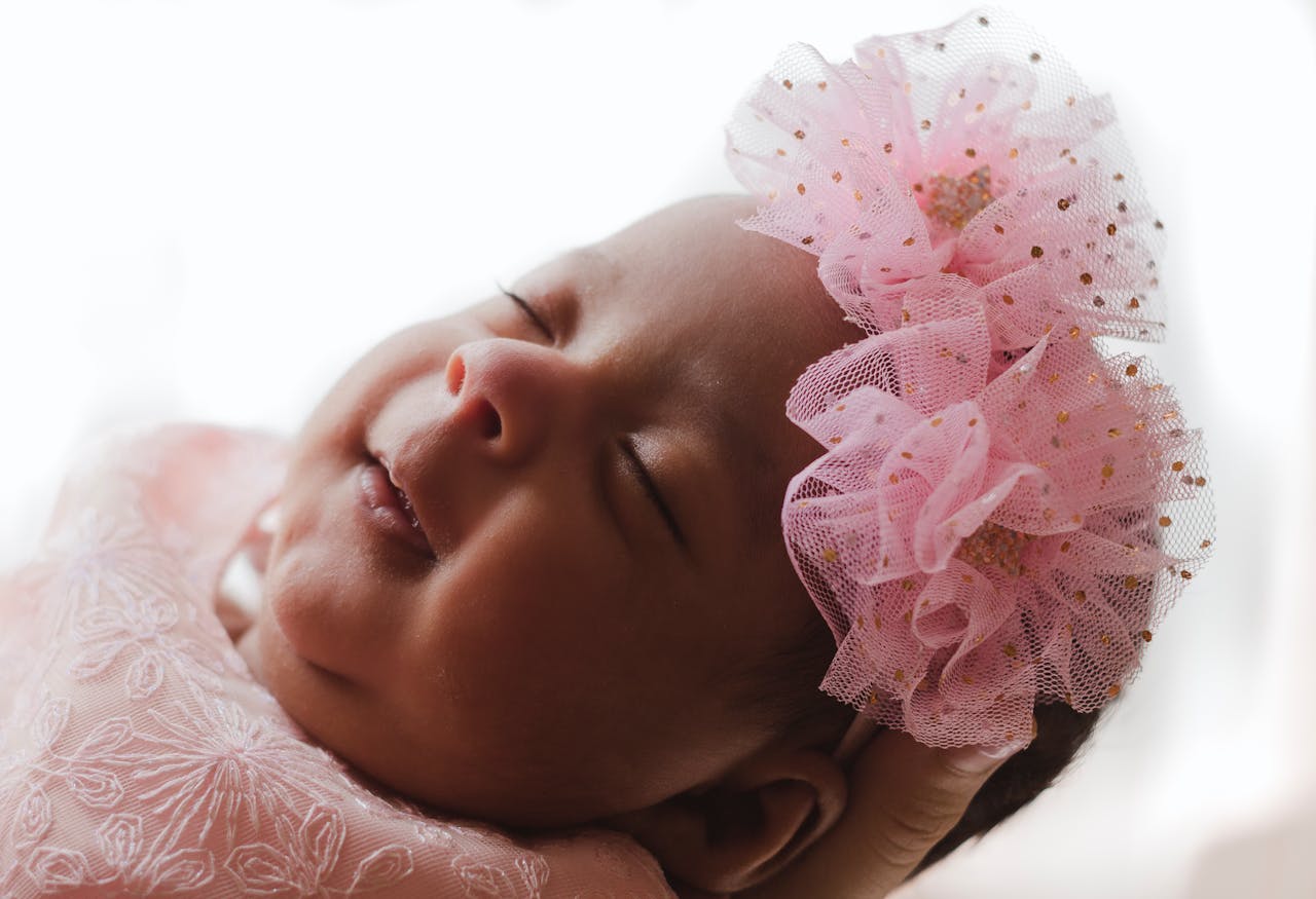 Close-up portrait of a peaceful baby sleeping with a pink floral headband.
