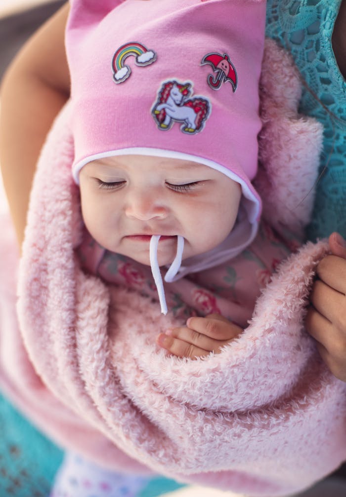 Close-up of an adorable baby wrapped in a soft pink blanket wearing a cute hat.